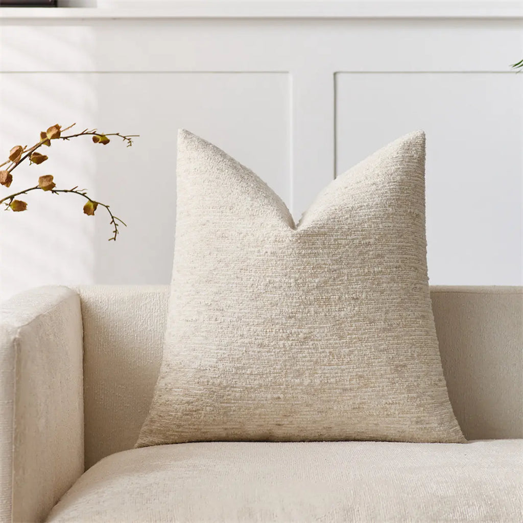 Beige textured pillow on a beige sofa with a white wall in the background