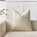 Beige textured pillow on a beige sofa with a white wall in the background