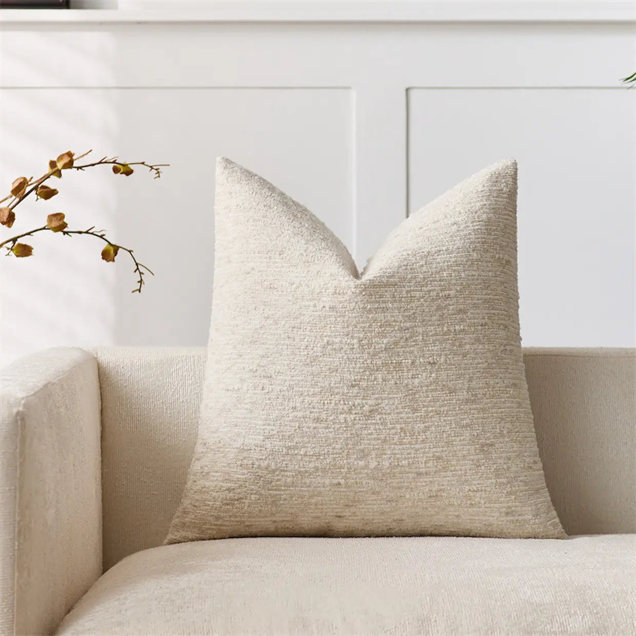 Beige textured pillow on a beige sofa with a white wall in the background